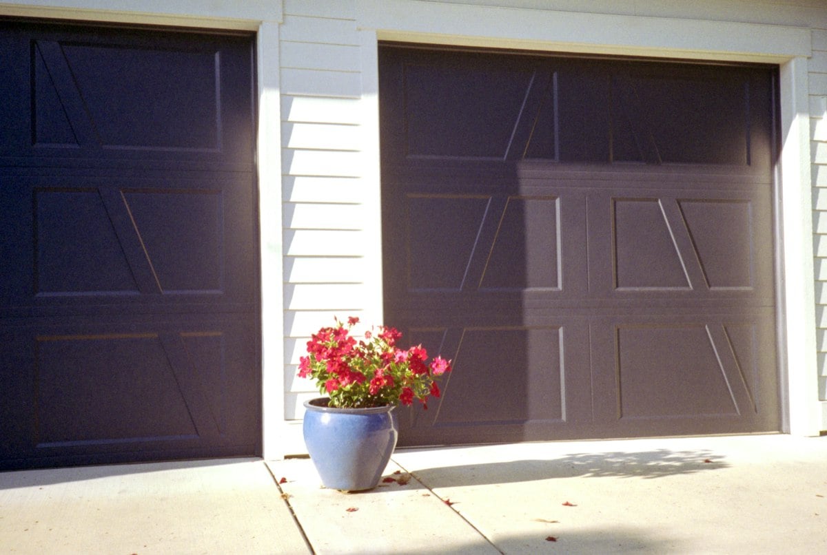 Brown paneled garage doors with a flower pot beside them